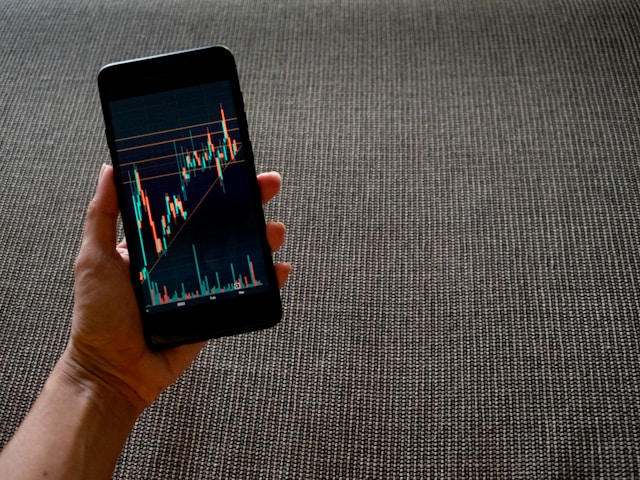 スマホを持って株式チャートを見ているイメージ